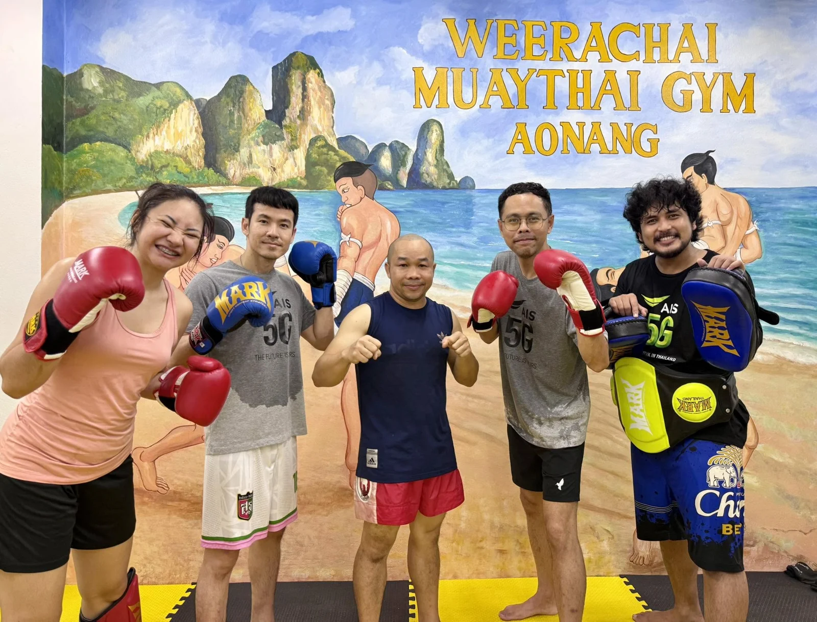 Five people smiling together with boxing gloves and pads at Weerachai Muaythai Gym
