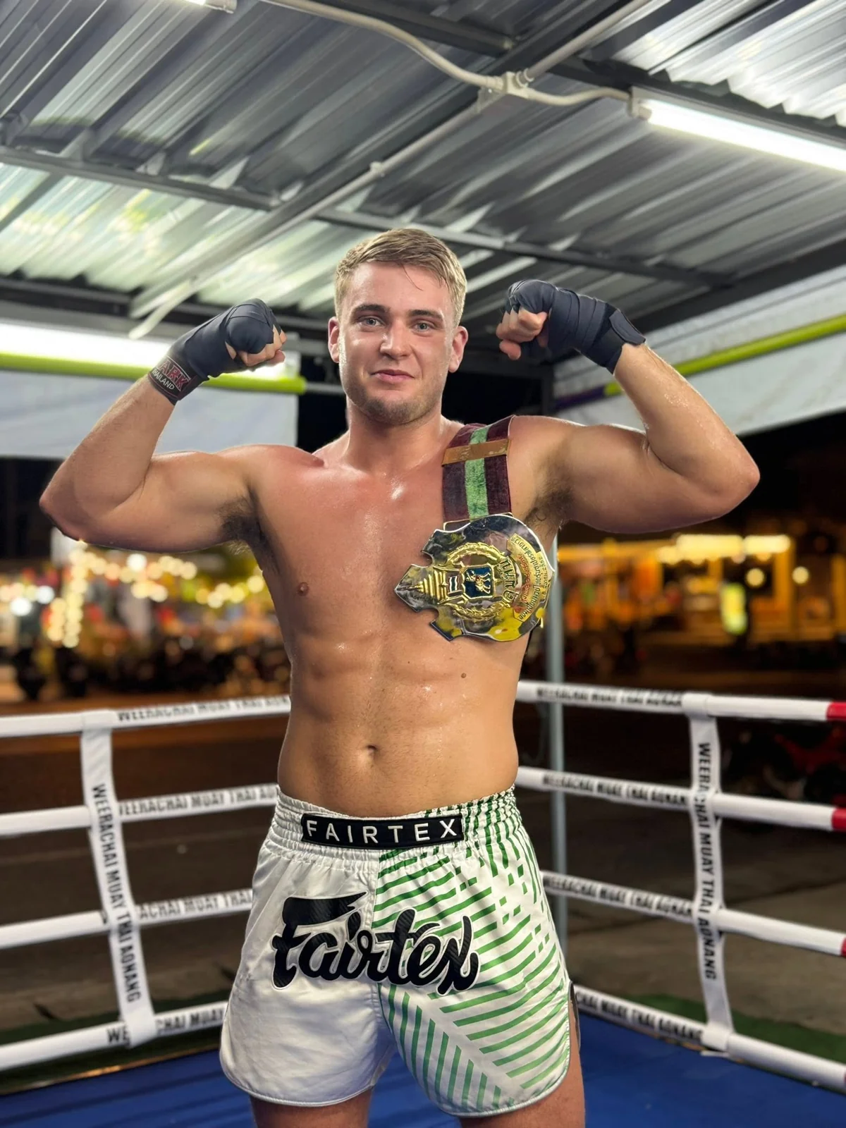 Boxer posing with gloves and a belt over his shoulder in a boxing ring
